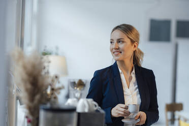 Smiling businesswoman holding coffee cup in office - JOSEF10009