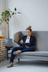 Businesswoman using tablet PC sitting on sofa at office - JOSEF10029