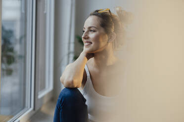 Lächelnde Frau schaut durch ein Fenster zu Hause - JOSEF10041