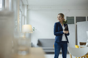 Smiling businesswoman holding plant in office - JOSEF10044