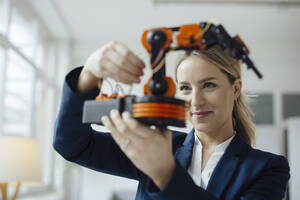 Smiling businesswoman analyzing robotic arm model in office - JOSEF10047