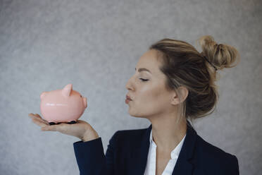 Businesswoman pouting in front of piggy bank at office - JOSEF10070