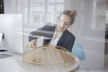 Businesswoman examining leaf shape model at desk seen through glass - JOSEF10093