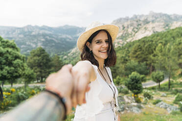 Young man holding happy girlfriend's hand in front of mountain range - DAMF00954