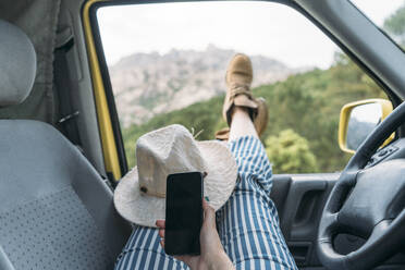 Hand einer Frau, die ein Mobiltelefon in einem Lieferwagen hält - DAMF00958