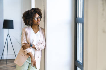 Smiling woman wearing blazer leaning on wall at workplace - VPIF06183