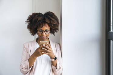 Woman using smart phone by white wall at workplace - VPIF06192