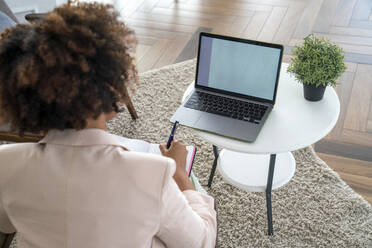 Young woman with laptop writing in diary at workplace - VPIF06223