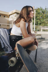Junge Frau mit Skateboard auf einer Bank sitzend - MRRF02120