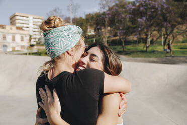 Glückliche Frau umarmt Freund im Skateboardpark an einem sonnigen Tag - MRRF02133
