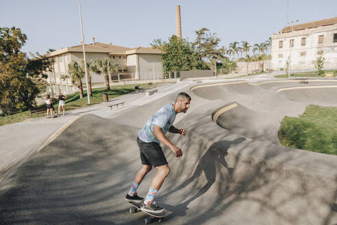 Mann fährt mit Freunden im Park Skateboard auf einer Sportrampe - MRRF02134