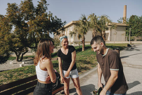 Lächelnder Mann mit Frauen im Skateboardpark an einem sonnigen Tag - MRRF02135