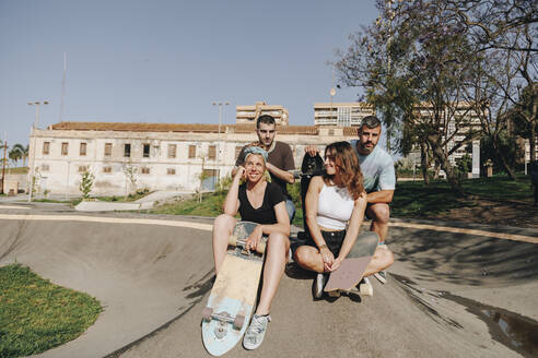 Lächelnde Freunde mit Skateboards auf einer Rampe an einem sonnigen Tag - MRRF02137