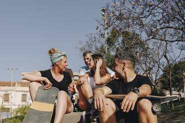 Freunde diskutieren miteinander, während sie in einem Skateboard-Park an einem sonnigen Tag sitzen - MRRF02140