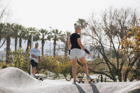 Lächelnde Frau mit Skateboard vor einem Freund auf einer Sportrampe - MRRF02144