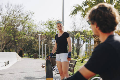 Frau hält Skateboard und sieht ihren Freund an einem sonnigen Tag an - MRRF02146