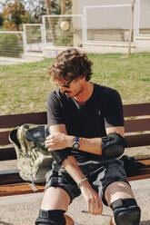 Mann auf einer Bank sitzend, der sein Ellbogenpolster im Park einstellt - MRRF02147