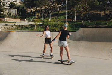 Happy women enjoying skateboarding at sports ramp on sunny day - MRRF02149