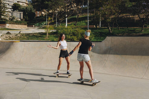 Glückliche Frauen genießen Skateboarding auf Sport-Rampe am sonnigen Tag - MRRF02149