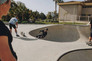 Mann fährt Skateboard auf Sportrampe inmitten von Freunden im Park - MRRF02151