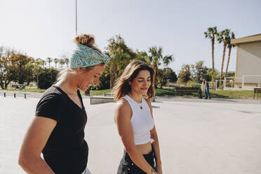 Happy friends talking at skateboard park on sunny day - MRRF02154