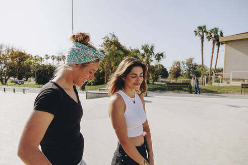 Glückliche Freunde unterhalten sich in einem Skateboard-Park an einem sonnigen Tag - MRRF02154