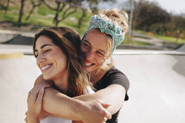 Lächelnde Frau umarmt Freund von hinten an einem sonnigen Tag - MRRF02155