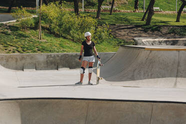 Frau in Sportschutzkleidung hält Skateboard auf Rampe - MRRF02163