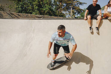 Ein Mann fährt Skateboard auf einer Sportrampe mit Freunden im Hintergrund - MRRF02166