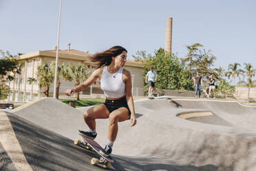 Junge Frau fährt Skateboard auf einer Sportrampe im Skatepark - MRRF02172