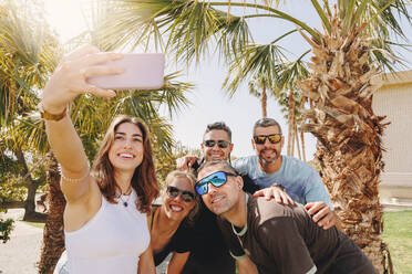 Smiling young woman with friends taking selfie through smart phone - MRRF02189