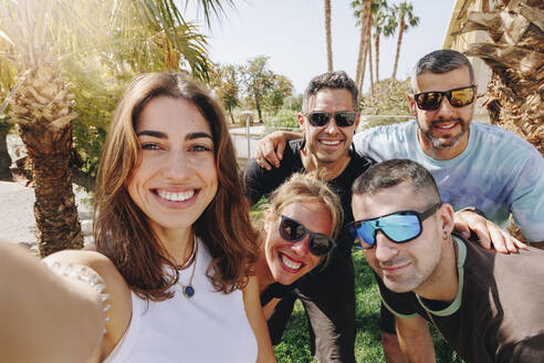 Lächelnde junge Frau macht Selfie mit Freunden an einem sonnigen Tag - MRRF02190