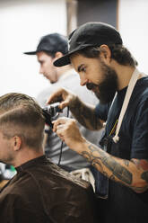 Junger Friseur, der mit einem elektrischen Rasiermesser die Haare eines Kunden im Salon schneidet - JUBF00422