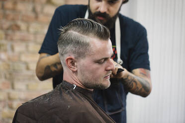 Junger Mann lässt sich vom Friseur im Salon die Haare schneiden - JUBF00423