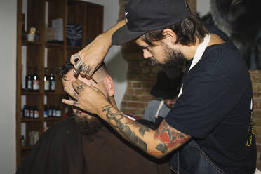 Mann im Friseursalon, der seinen Bart mit einer Rasierklinge rasiert - JUBF00429