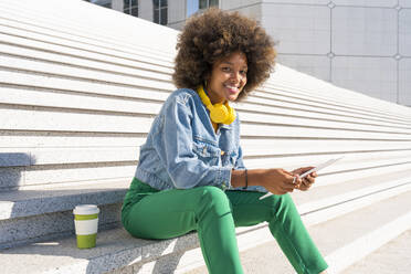 Lächelnde junge Afro-Frau mit Tablet-PC auf einer Treppe sitzend - OIPF01790