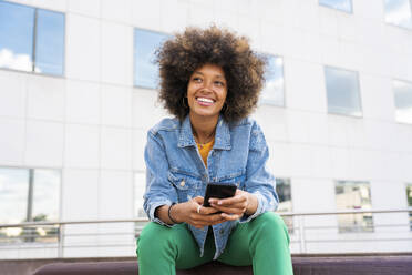 Schöne glückliche Frau mit Afro-Frisur hält Handy sitzen auf Bank - OIPF01826