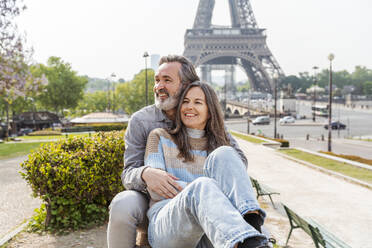 Fröhlicher reifer Mann und Frau sitzen zusammen im Park vor dem Eiffelturm, Paris, Frankreich - OIPF01840