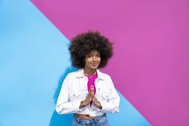 Afro-Frau steht mit verschränkten Händen vor einer rosa und blauen Wand - OIPF01845