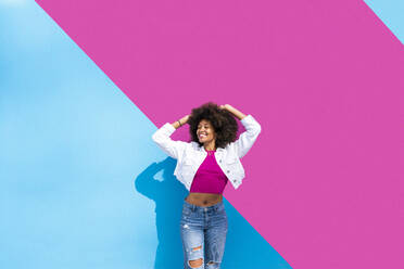Happy woman with eyes closed enjoying in front of pink and blue wall - OIPF01849