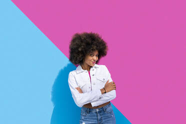 Smiling young woman with arms crossed in front of pink and blue wall - OIPF01850