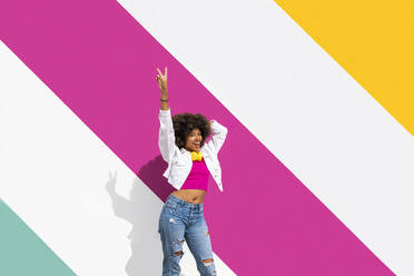 Happy young woman standing with hand raised in front of colorful wall - OIPF01864