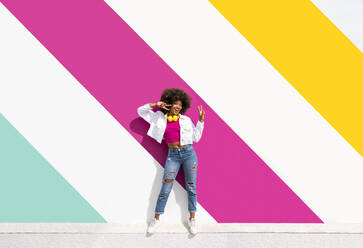 Happy woman gesturing peace sign in front of colorful wall - OIPF01869