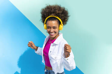 Glückliche Frau hört Musik über drahtlose Kopfhörer und tanzt vor einer blauen Wand - OIPF01887