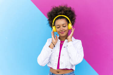 Lächelnde junge Frau mit geschlossenen Augen genießt Musik hören durch vor rosa und blauen Wand - OIPF01888