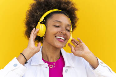 Junge Frau mit geschlossenen Augen genießt Musik vor einer gelben Wand - OIPF01890