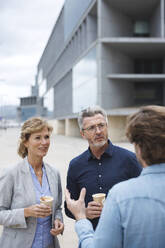 Businessman discussing with colleagues holding disposable coffee cups - JOSEF10099