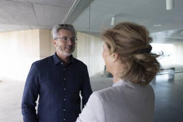 Smiling businessman talking with colleague standing by glass wall - JOSEF10103