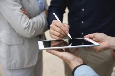 Hand eines Geschäftsmannes, der auf einem Tablet-PC unterschreibt und neben Kollegen steht - JOSEF10110