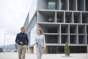 Businessman discussing with businesswoman walking in front of office building - JOSEF10114